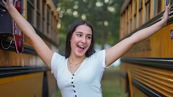 Una joven con cabello oscuro está con los brazos en alto frente a un fondo colorido en el terreno de la Saint Paul Lutheran High School.