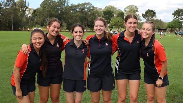 Un grupo de jóvenes estudiantes está en ropa deportiva en un campo de césped en el campus del Saint Stephen’s College.