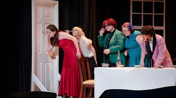 Un grupo de personas está de pie en coloridos atuendos en el escenario de la Salem Academy frente a una mesa blanca.