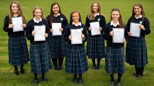 Un grupo de alumnas de la Salerno Secondary School está en un campo de césped sosteniendo certificados en las manos.