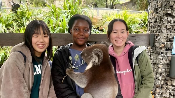 Tres estudiantes de la Salisbury East High School están frente a un jardín verde y conversan amablemente.