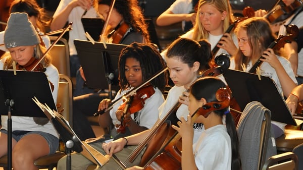 Un grupo de estudiantes de la Salmo Secondary School toca diferentes instrumentos de cuerda en el escenario frente a una audiencia.