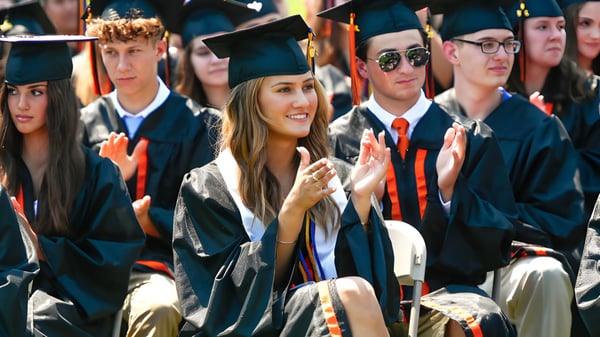 Graduadas y graduados de la Samuel Robertson Secondary School están juntos en toga de graduación y sonríen a la cámara.