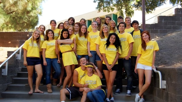 Un grupo de alumnas de la San Luis Obispo High School se sienta en escaleras exteriores frente a un edificio y árboles.