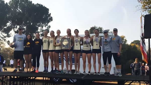 Un grupo de jóvenes atletas de la San Luis Obispo High School se encuentra con trofeos en un escenario frente a árboles y un cielo despejado.