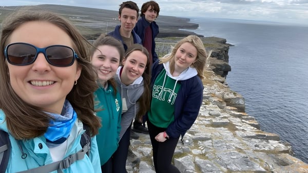 Un grupo de alumnas y alumnos del Sancta Maria College se toma un selfie frente a un paisaje costero con acantilados y mar de fondo.