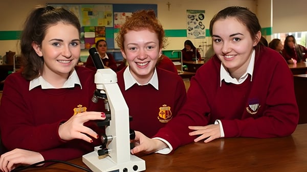 Tres alumnas en uniforme escolar están juntas y sonríen en un aula del Sancta Maria College Ballyroan.
