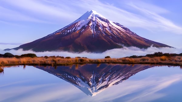 Una montaña nevada se refleja en un lago tranquilo con vegetación frente al Sancta Maria College.