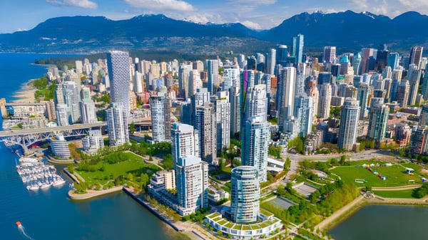 Vista de la línea del horizonte urbano con rascacielos y un parque desde el terreno de la Sands Secondary School en el puerto frente a montañas.