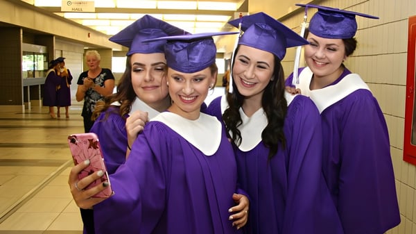 Estudiantes de la Sandwich Secondary School posan con togas de graduación moradas para un selfie en el pasillo.