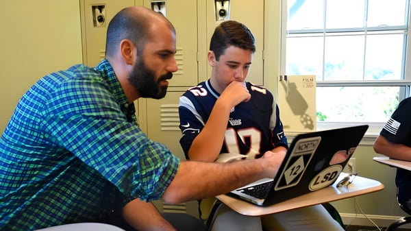 Un hombre con barba y un estudiante están sentados juntos en el portátil en el campus de la Sandy Spring Friends School.