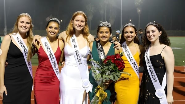 Un grupo de jóvenes mujeres vestidas de gala posan juntas en un escenario en el terreno de la Santa Barbara High School.