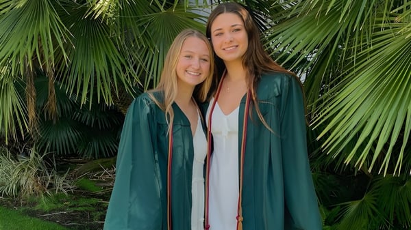 Dos estudiantes están juntas en un entorno tropical con grandes hojas de palma en el terreno del Santa Barbara Unified School District.