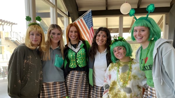 Un grupo de mujeres en ropa festiva posa frente a una bandera americana en el campus de la Santa Catalina School.