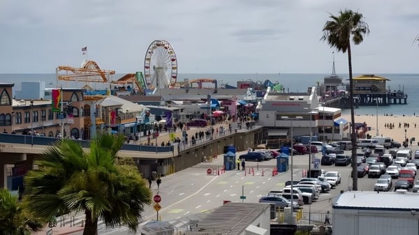 Estudiantes del Santa Monica College caminan a lo largo del bullicioso paseo marítimo con la noria y atracciones de parque de diversiones junto al mar.