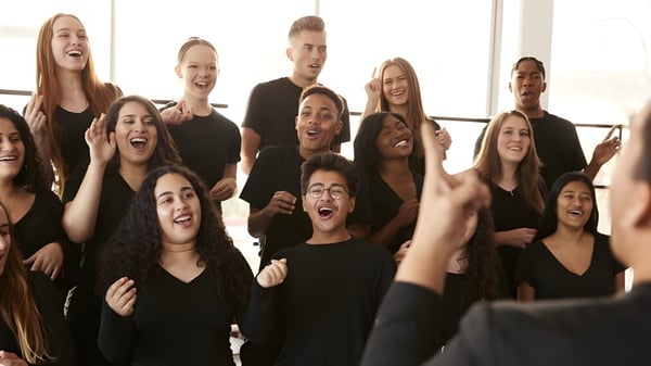 Un grupo de estudiantes de la Santiam Christian School se muestra expresivo frente a un brillante fondo natural y levanta las manos.