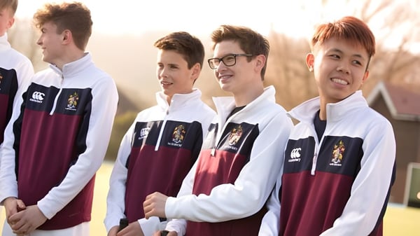 Un grupo de estudiantes de Scarborough College está al aire libre en uniformes escolares con camisas blancas y suéteres burdeos.