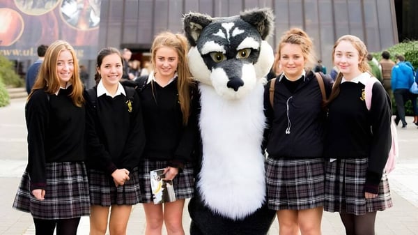 Estudiantes de Scoil Aireagail están juntos con un gran animal parecido a un lobo blanco y gris en primer plano.
