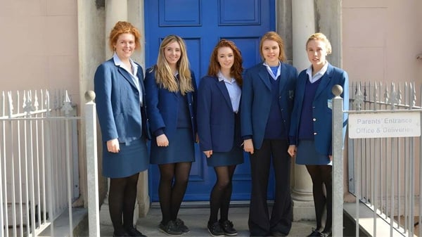 Cinco estudiantes de la Scoil Mhuire Cork están en uniformes azules frente a una puerta azul brillante.