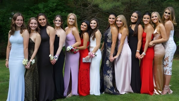 Un grupo de jóvenes mujeres en ropa formal está reunido en el área verde exterior de la Scoil Mhuire Cork.