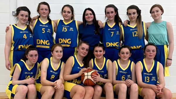 Un grupo de jóvenes estudiantes de la Scoil Mhuire Kanturk posan como equipo de baloncesto con una pelota frente a una pared sencilla.