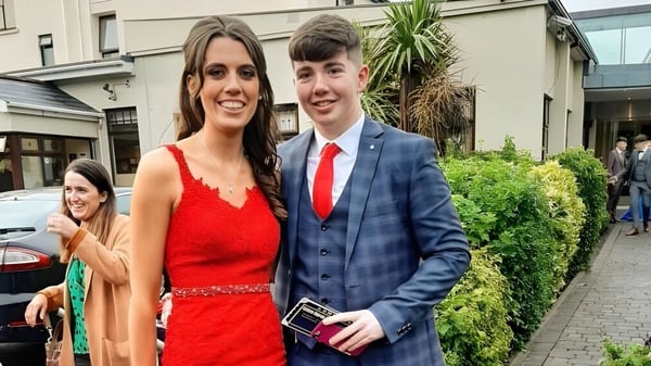 Una joven pareja está frente a un edificio con plantas verdes en el terreno de Scoil Mhuire (Strokestown).