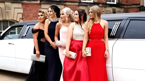 Estudiantes de la Scoil Ruáin están frente a una limousine blanca delante de un edificio de ladrillo.