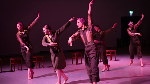 Un grupo de estudiantes del Seaford College baila sincronizadamente en el escenario en una sala iluminada en rosa-violeta.