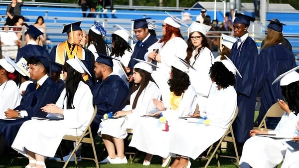 Un grupo de graduados de la Seaford Head School está al aire libre en ropa académica con birretes en un día soleado.