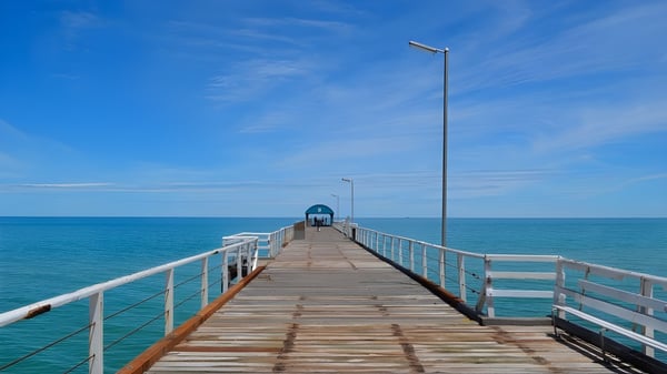 Un muelle de madera se extiende sobre el mar tranquilo y turquesa bajo un cielo despejado en el campus de la Seaton High School.