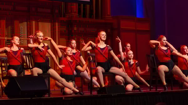 Un grupo de jóvenes bailarinas de la Seaview High School se presenta en un escenario con iluminación roja y azul.