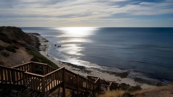 Una escalera de madera lleva a la playa con suaves olas bajo un cielo nublado en el terreno de la Seaview High School.