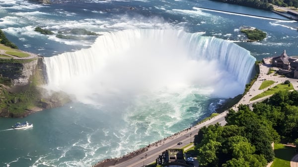 Una cascada fluye sobre un acantilado rocoso con un entorno verde y un río al fondo cerca de Seaway District High School.