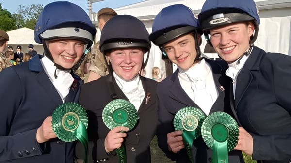 Cuatro hombres en ropa formal con cascos de equitación sostienen rosetas verdes en un evento en el terreno de la Sedbergh School.