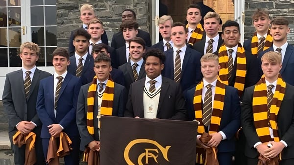 Un grupo de estudiantes de la Sedbergh School está frente a un edificio escolar de piedra en uniformes escolares con trajes y bufandas a rayas.