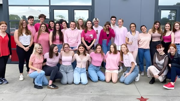 Un grupo de jóvenes mujeres en diferentes tonos de rosa posan frente a un edificio moderno en el Selwyn College.