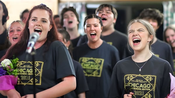Un grupo de alumnas y alumnos del Selwyn College canta juntos vestidos con camisetas negras de Chicago.