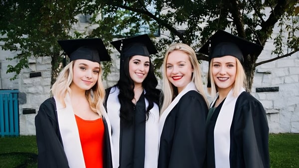 Cuatro egresadas del Séminaire de Chicoutimi posan juntas frente a un fondo boscoso.