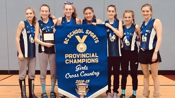 Estudiantes de la Sentinel Secondary School sostienen orgullosamente un banner como campeonas provinciales en el cross femenino de la temporada 2018-19.