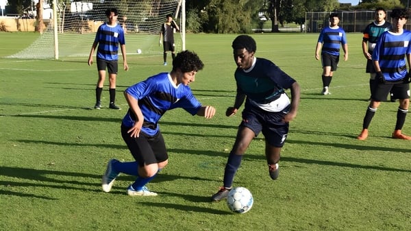 Un grupo de jugadores de fútbol en uniforme azul y negro juega un partido en el campo deportivo del Sevenoaks Senior College.