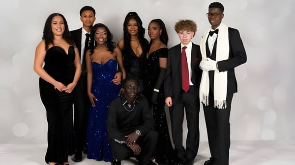 Un grupo de personas vestidas de manera formal está de pie frente a un fondo blanco en el campus del Sevenoaks Senior College.