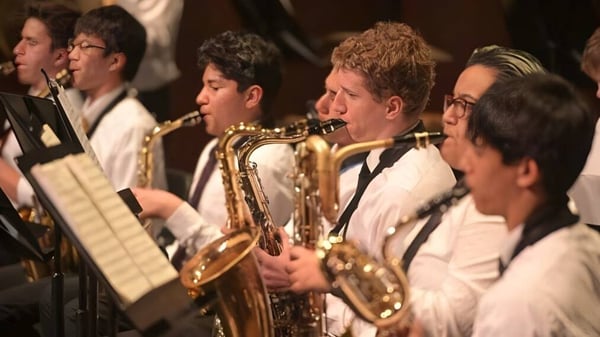 Un grupo de estudiantes de música de la Shady Side Academy toca instrumentos de viento en un escenario con ropa formal.