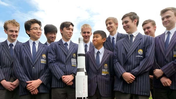 Un grupo de jóvenes del Sheldon College está junto en trajes azul oscuro frente a un cielo nublado.