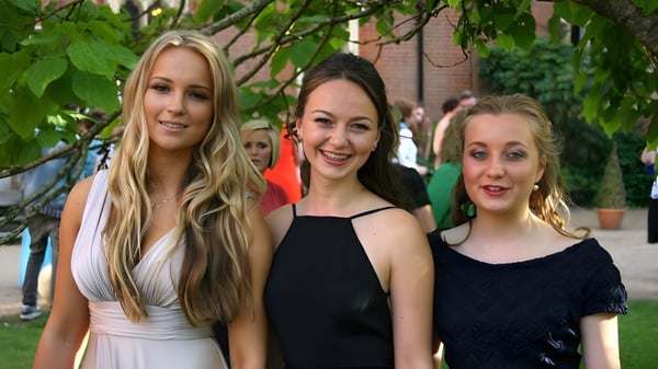 Tres escolares de la Sherborne Girls' School están juntas en un jardín con exuberante vegetación y árboles.