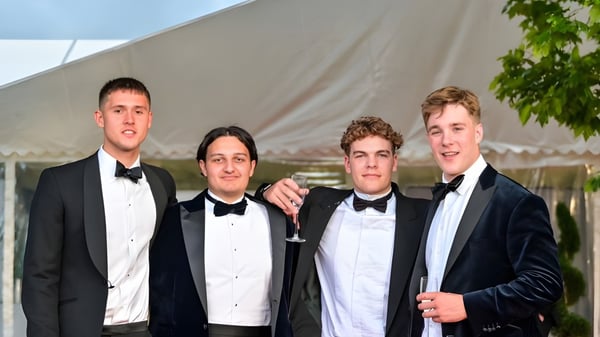 Cuatro estudiantes de la Sherborne School en ropa formal posan juntos frente a una carpa y un entorno verde.