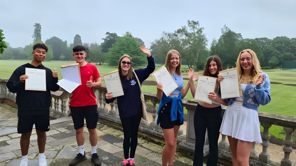 Estudiantes de la Sherfield School están al aire libre sosteniendo sus certificados frente a un paisaje verde.