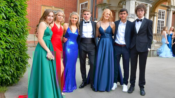 Un grupo de personas elegantemente vestidas se encuentra frente al edificio de ladrillo de la Sherfield School con un fondo verde.