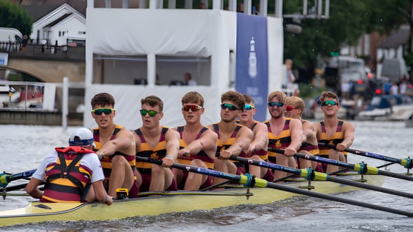 Un grupo de remeros en uniformes coloridos está sentado en un barco en el agua en el terreno del Shiplake College.