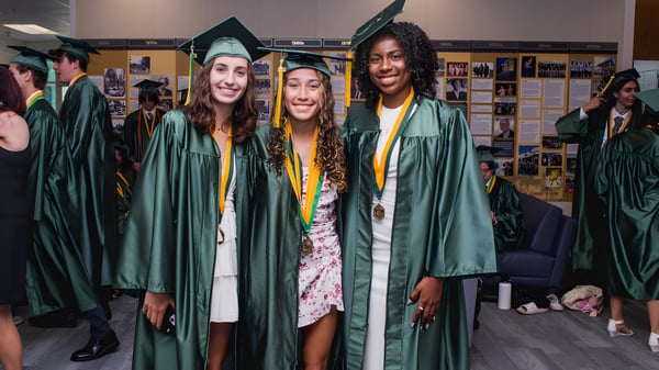 Un grupo de graduados de la Shorecrest Preparatory School se encuentra en el pasillo de la escuela con togas y birretes verdes.