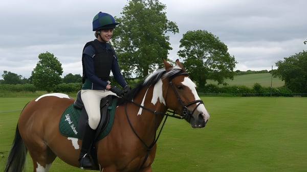 Una estudiante de la Sibford School está vestida de equitación montando un caballo marrón y blanco en un prado.